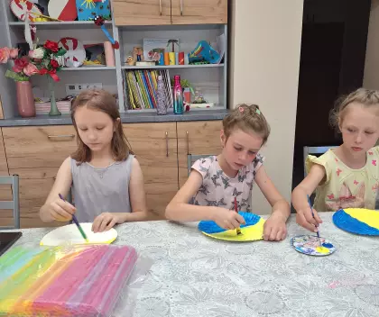 Dziewczynki malują farbami talerzyk papierowy.