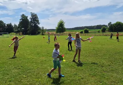 Dzieci biegają po boisku i puszczają latawce.