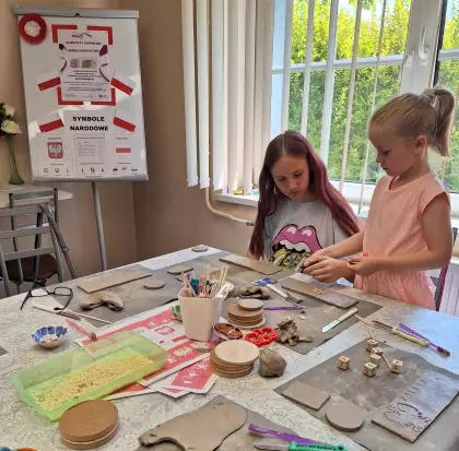 Dziewczyny siedzą przy stole i wyciskają symbole narodowe na kubku ceramicznym.