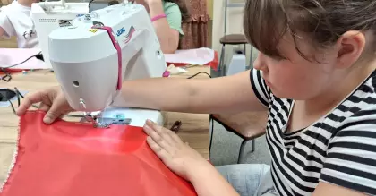 Dziewczynka szyje flagę Polski na maszynie.