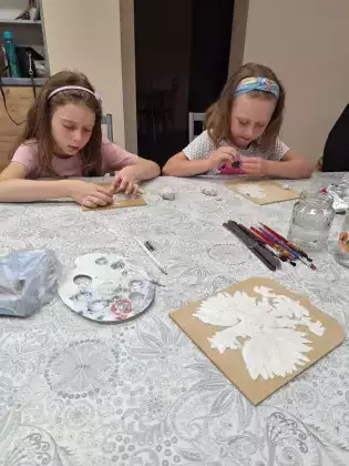 Dziewczynki siedzą przy stole i wykonują godło polski.