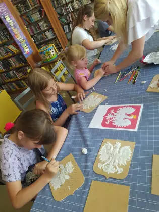 Uczestnicy zajęć patriotycznych wyklejają masą modelarską orzełka.