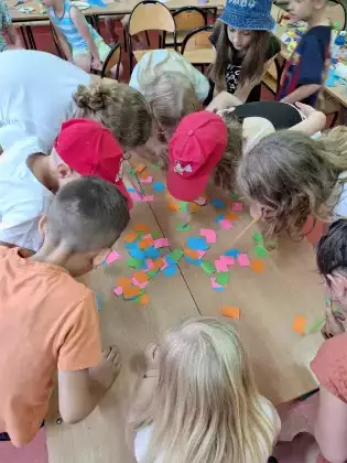 Dzieci bawią się w zbieranie kolorowych papierków rurką plastikową.