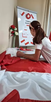 Uczestniczka warsztatów szyje flagę Polski.