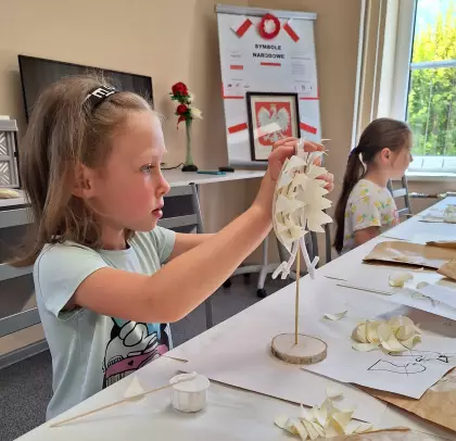 Dziewczynka wykleja osikowymi wiórkami statuetkę orzełka.