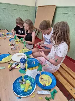 Uczestnicy na talerzykach papierowych przyklejają palmy.