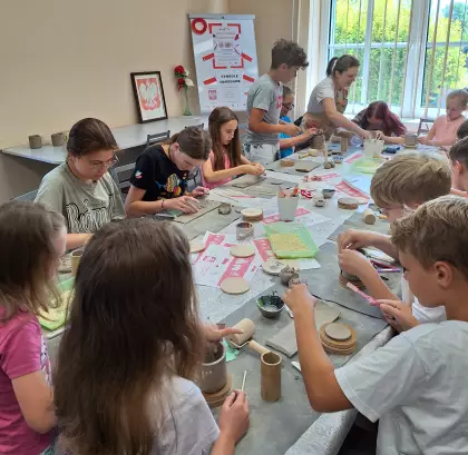 Uczestnicy warsztatów przy wspólnym stole wykonują kubki z gliny.