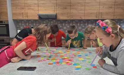 Dzieci bawią się w zbieranie kolorowych karteczek słomkami.