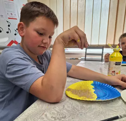 Chłopak sypie piaskiem pomalowany farbami talerzy.