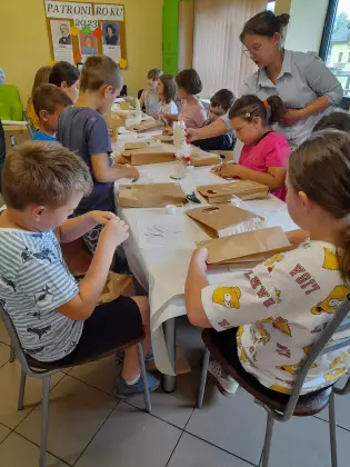 Dzieci siedzą przy stoliku i wykonują pracę plastyczną.