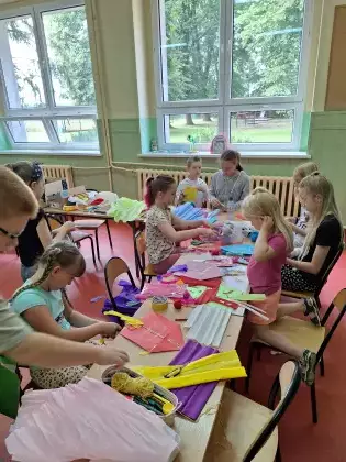 Uczestnicy zajęć kleją kolorowe latawce z papieru.