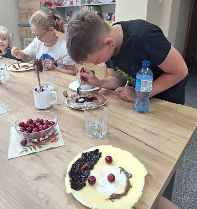 Dzieci ozdabiają naleśniki dżemem i  owocami.