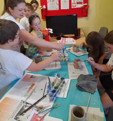 Uczestnicy spotkania malują kubki farbą ceramiczną.