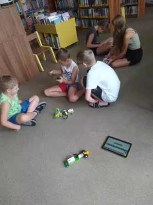 Dzieci siedzą na podłodzi i jeżdżą pojazdami z lego.