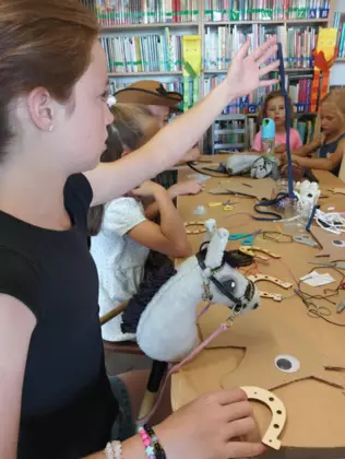 Dzieci siedzą przy stoliku i wykonują prace plastyczne.