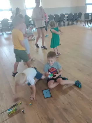 Uczestnicy jeżdżą zbudowanymi pojazdami z klocków lego po bibliotece.