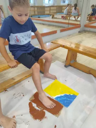 Chłopczyk odbija stopę pomalowaną farbą na kartce papieru.