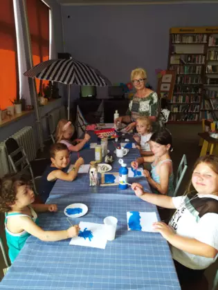 Dzieci siedzą przy stole i malują farbami.