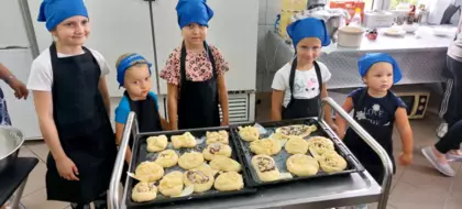 Dzieci pozują z gotowymi do wypieku ciastkami drożdżowymi (kołoczkami).