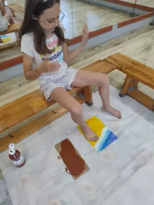 Dziewczynka odbija pomalowaną stopę na kartkę.