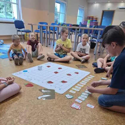 Dzieci wraz z instruktorką siedzą na podłodze i programują Genibota.