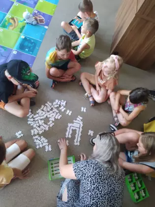 Grupka dzieci układa ze specjalnych  puzzli trasę dla Ozobota.