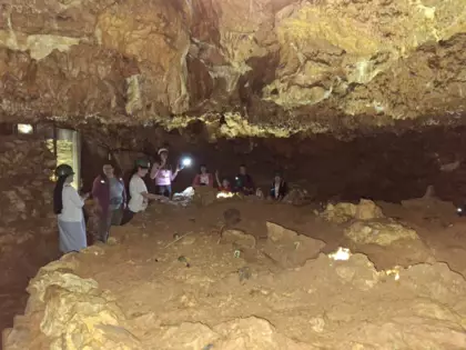 Uczestnicy we wnętrzu Jaskini Głębokiej słuchają przewodniczki.