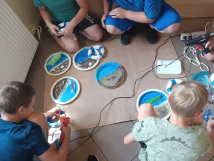 Dzieci przyklejaja muszelki i koła ratunkowe do swoich prac wakacyjnych.