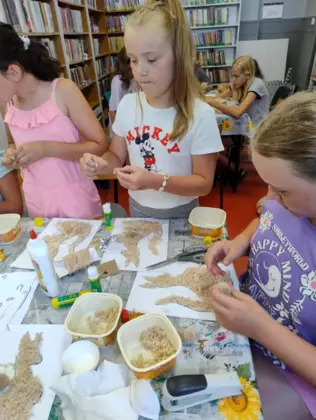 Uczestnicy zajęć tną wełnę na malutkie kawałki i wyklejają nią kangurki.