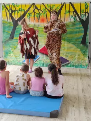 Dzieci siedzą na materacu i oglądają teatrzyk.