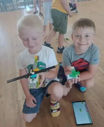 Dwóch chłopców przedstawiają zbudowane przez siebie maszyny jeżdżące z klocków lego.