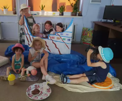 Wspólne zdjęcie dzieci z panią bibliotekarką zrobione pod parasolem w statku z kartonu.