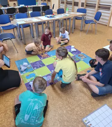 Dzieci wraz z instruktorką siedzą na podłodze i programują Photona.