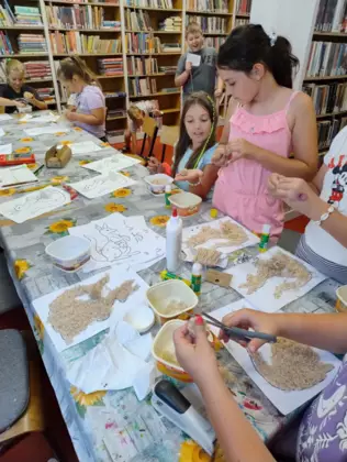 Uczestnicy zajęć tną wełnę na malutkie kawałki i wyklejają nią kangurki.
