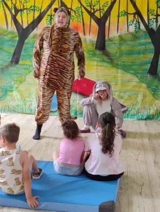 Dzieci siedzą na materacu i oglądają teatrzyk.