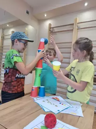 Chłopcy układają wieżę z kubków według podanego schematu.