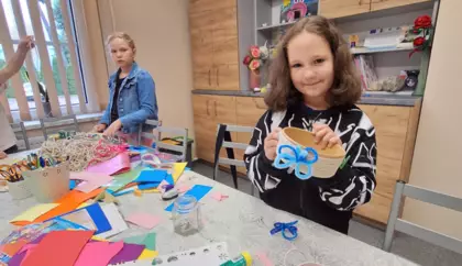 Dziewczynka przykleja motylka do koszyczka. w tyle dziewczyna rozwija sznurek.