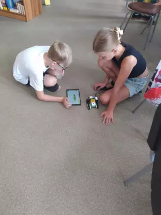 Dziewczynka i chłopak na tablecie programują pojazdy złożone z klocków.