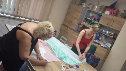 Uczestniczki warsztatów wycinają nożyczkami ubranie z materiału.
