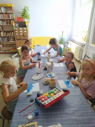 Dzieci siedzą przy stole i malują farbami.