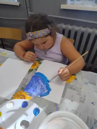 Dziewczynka maluje farbami obrazek wakacyjny.