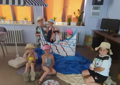 Wspólne zdjęcie dzieci z panią bibliotekarką zrobione pod parasolem w statku z kartonu.