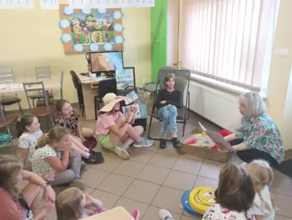Dzieci siedzą na podłodze i słuchają czytanej książki przez panią bibliotekarkę