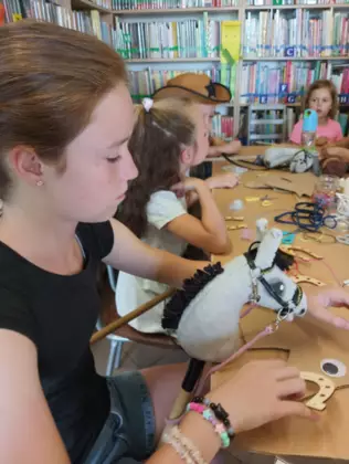 Dzieci siedzą przy stoliku i wykonują prace plastyczne.