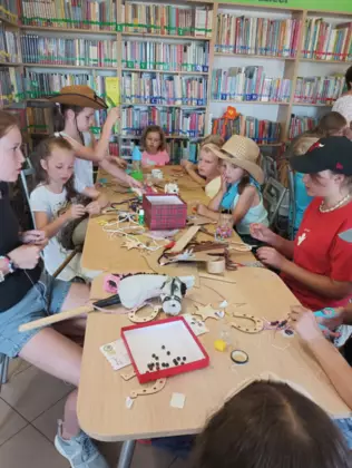 Dzieci siedzą w bibliotece i wykonują prace plastyczne.