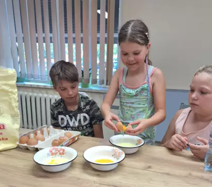 Dwie dziewczynki i chłopczyk rozbijają jajka do jagodzianek.