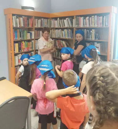 Pani bibliotekarka pokazuje uczestnikom zajęć, gdzie  w bibliotece znajdują się książki kucharskie.