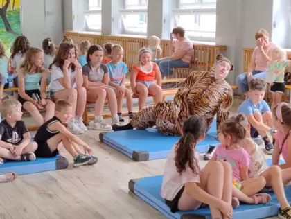 Dzieci siedzą na ławeczkach i oglądają przedstawienie teatralne.