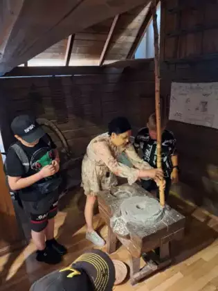 Przewodniczka pokazuje dwóm chłopakom jak działa maszyna do mielenia ziarna.