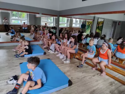 Dzieci siedzą na ławeczkach i oglądają przedstawienie teatralne.